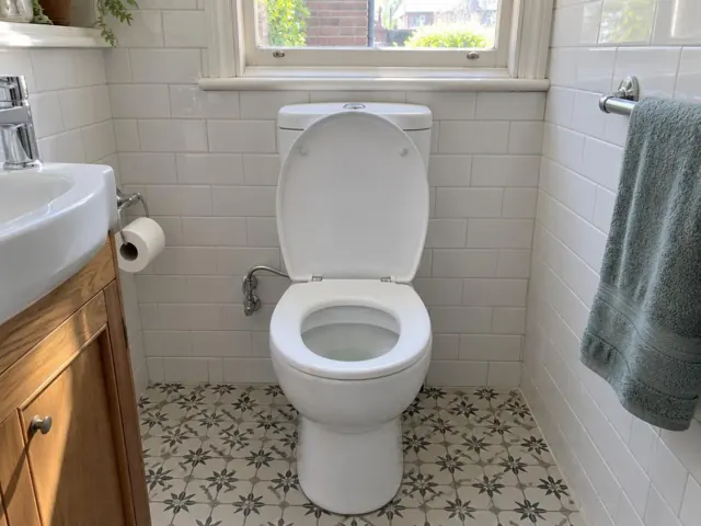 Clean white toilet in a tiled bathroom with patterned floor and window in Botany