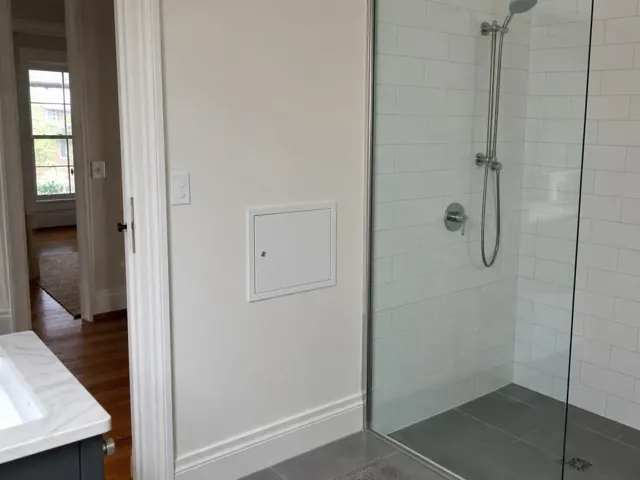 Bathroom wall with small access panel beside a tiled shower and glass screen in Botany
